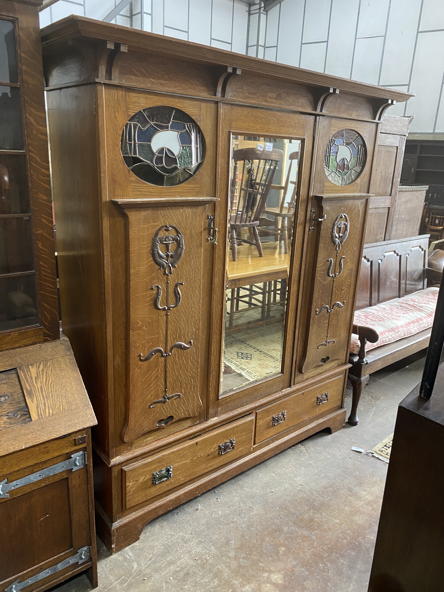 An Arts & Crafts copper and brass mounted oak compactum wardrobe in the style of Shapland & Petter, inset oval stained glass panels, width 185cm, depth 58cm, height 203cm